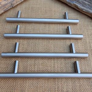 May include: Four brushed nickel cabinet pulls with a simple, modern design. Each pull is approximately 5 inches long.