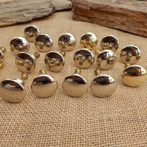 May include: A collection of 20 round cabinet knobs in two finishes: polished nickel and gold. The knobs have a smooth, shiny surface and are arranged in a semi-circle on a burlap background.