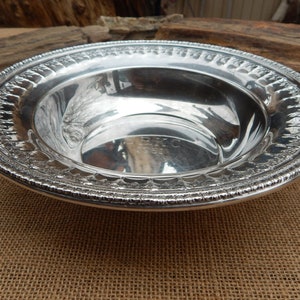 May include: A silver serving bowl with a decorative embossed rim. The bowl is round and has a smooth, reflective surface.