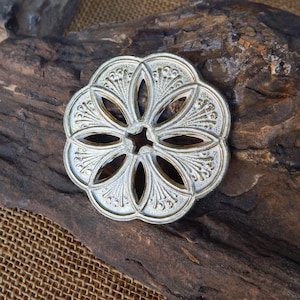 May include: A silver and gold decorative metal medallion with a floral design and cut-out details.