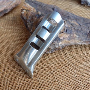 May include: A silver metal bracket with three slots. The bracket is designed to hold a variety of items, such as pipes or wires.