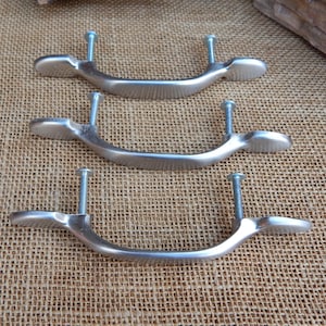 May include: Three silver cabinet pulls with rounded ends and a curved shape. The pulls have a brushed finish and are attached to screws.