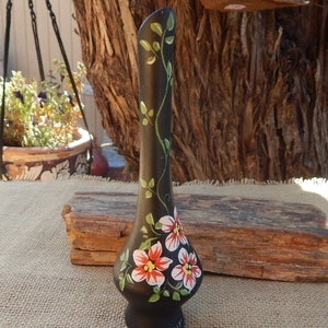 May include: Black ceramic vase with a long, slender neck and a bulbous base. The vase is hand-painted with green vines and red, white, and orange flowers. The vase is signed "oswaldi" on the bottom.