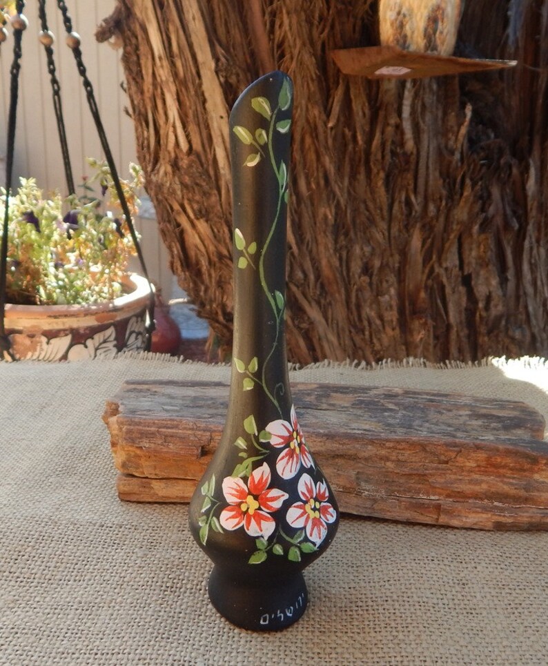 May include: Black ceramic vase with a long, slender neck and a bulbous base. The vase is hand-painted with green vines and red, white, and orange flowers. The vase is signed "oswaldi" on the bottom.