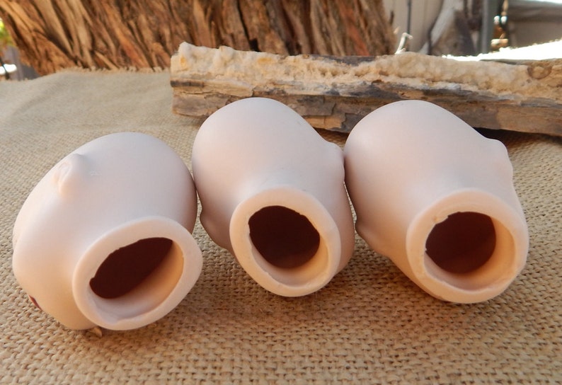 May include: Three unfinished porcelain doll heads, each with a round opening at the bottom. The heads are light pink and have a smooth, matte finish.