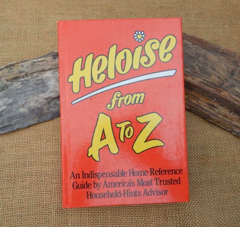 May include: A vintage book titled "Heloise from A to Z" with a bright red cover and yellow lettering. The book is a home reference guide, as stated on the cover. A daisy graphic is above the title.