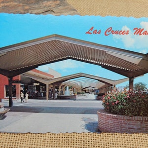 May include: A vintage postcard featuring a view of the Las Cruces Mall, a covered shopping center with a fountain in the middle. The postcard has a blue sky with white clouds and a red title that reads "Las Cruces Mall".
