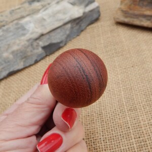May include: A close-up of a round, wooden ball with a reddish-brown color and dark brown streaks. The ball has a smooth, polished surface.