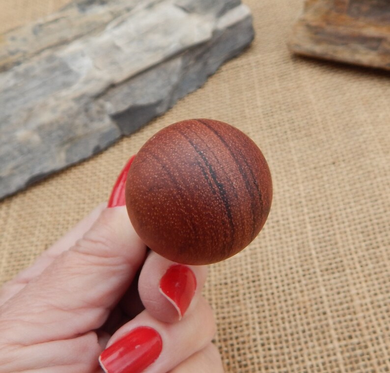 May include: A close-up of a round, wooden ball with a reddish-brown color and dark brown streaks. The ball has a smooth, polished surface.
