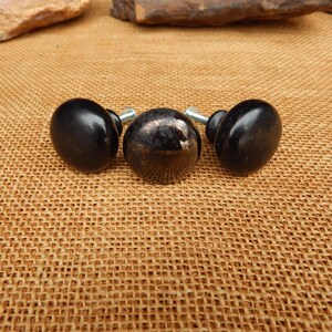 May include: Three black cabinet knobs with a glossy finish. The knobs are oval-shaped and have a silver screw post. The center knob has a speckled, reflective surface. These knobs are suitable for furniture restoration or DIY projects.