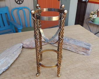 May include: A gold metal decorative stand with a round top and three legs. The stand has a twisted rope design and is made of metal.