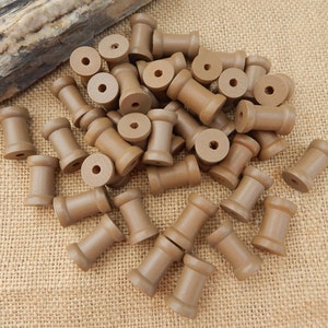 May include: A pile of brown wooden spools, perfect for crafting projects. The spools are about 1 inch in diameter and 1 inch tall.