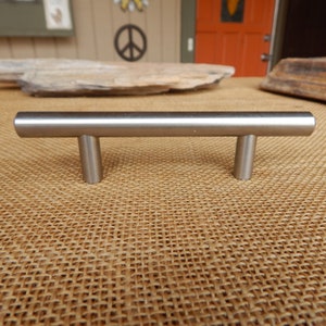 May include: A brushed nickel cabinet pull with a rectangular bar and rounded ends. The pull is approximately 3 inches long.
