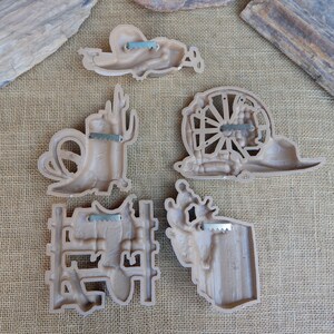 May include: Set of six brown plastic wall decor pieces with a western theme. The pieces include a cactus, a horseshoe, a wagon wheel, a cowboy boot, a cowboy hat, and a steer skull.