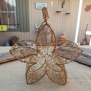 Könnte beinhalten: Goldfarbener Drahtkorb in Blumenform mit einem gedrehten Drahtgriff. Der Korb besteht aus einem filigranen Drahtgeflecht und hat ein sternenförmiges Design.
