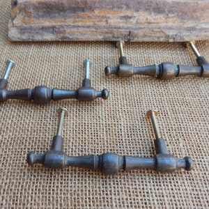 May include: Four antique-style cabinet drawer pulls with a dark bronze finish. Each pull has a rounded, slightly curved design with a center knob and two screw holes.