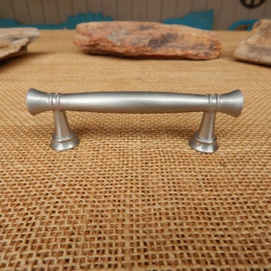 May include: A silver cabinet pull with a rounded rectangular shape and a slightly flared design at each end.