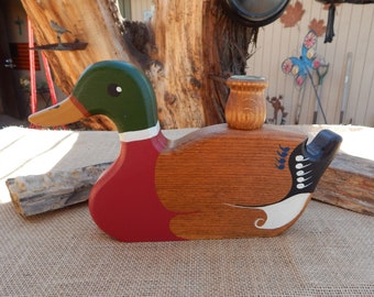 Könnte beinhalten: Kerzenhalter aus Holz in Form einer Ente, bemalt in den Farben Rot, Grün, Braun, Weiß und Blau. Die Ente hat einen kleinen Kerzenhalter auf dem Rücken.