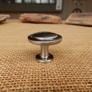 May include: A silver round cabinet knob with a raised edge and a smooth, shiny finish.