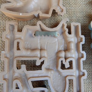 May include: A beige plastic wall decor with a metal hanging hook. The decor is shaped like a castle with a tower and a gate. The decor has a textured surface.