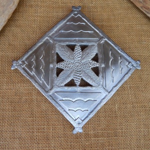 May include: A silver metal decorative wall hanging with a geometric design. The design features a star in the center and wavy lines around the edges.