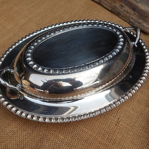May include: A silver oval serving dish with a lid and two handles. The dish has a beaded edge.