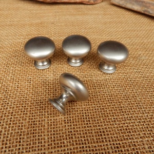 May include: Four silver cabinet knobs with a round, slightly domed shape. The knobs have a smooth, polished finish.