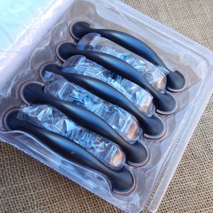 May include: A package of eight black cabinet pulls with a brushed nickel finish. The pulls are packaged in a clear plastic clamshell.