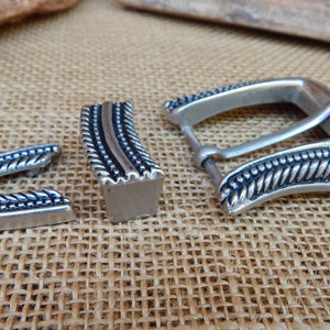 K&ouml;nnte beinhalten: Silberne G&uuml;rtelschnalle mit einem Seil-Design. Die Schnalle ist aus Metall und hat eine polierte Oberfl&auml;che.