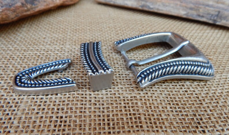 K&ouml;nnte beinhalten: Silberne G&uuml;rtelschnalle mit einem Seil-Design. Die Schnalle ist aus Metall und hat eine polierte Oberfl&auml;che.