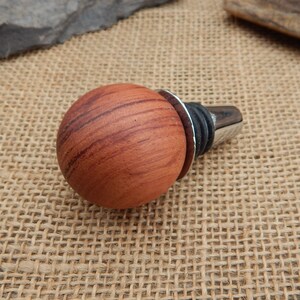 May include: A wooden bottle stopper with a round, reddish-brown top and a silver metal base.