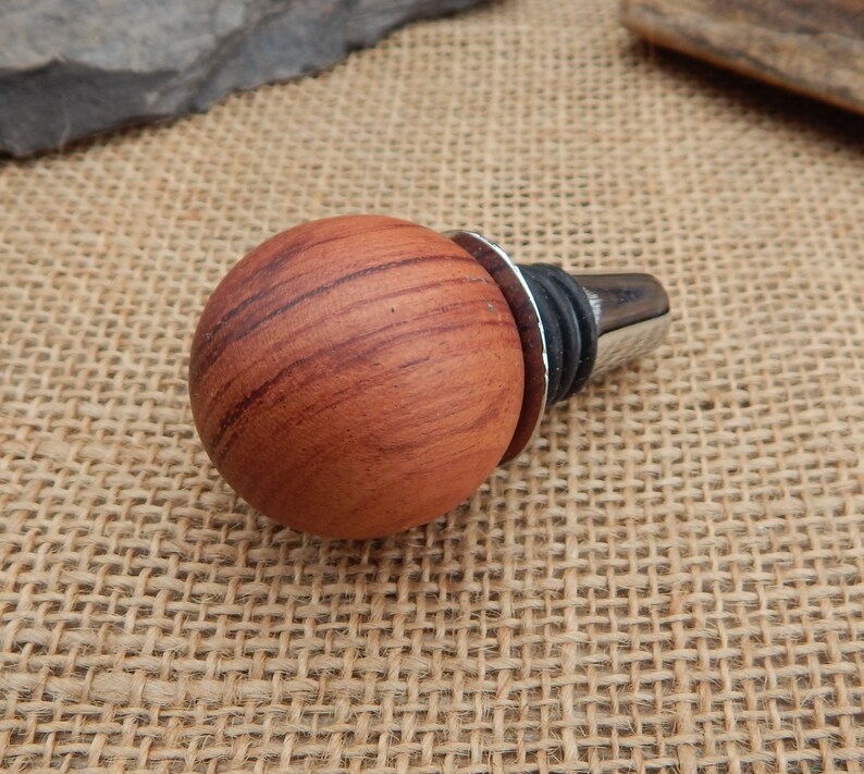 May include: A wooden bottle stopper with a round, reddish-brown top and a silver metal base.