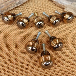 May include: Ten round, gold and black cabinet knobs with a decorative band around the middle. The knobs have a shiny finish.