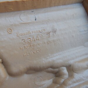 May include: Close-up of a brown plastic toy with the text "Buckwood Prod. Co. 3344-3 Made in U.S.A. MCMXCV" printed on the bottom.
