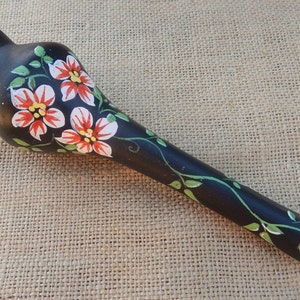 May include: A black ceramic vase with a long, slender neck and a bulbous base. The vase is hand-painted with white and red flowers and green leaves. The vase is signed "04/11".