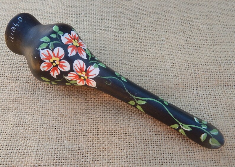 May include: A black ceramic vase with a long, slender neck and a bulbous base. The vase is hand-painted with white and red flowers and green leaves. The vase is signed "04/11".