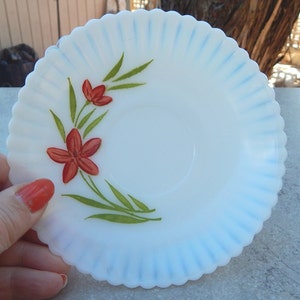 May include: White milk glass saucer with a blue rim and a hand-painted design of red flowers and green leaves.