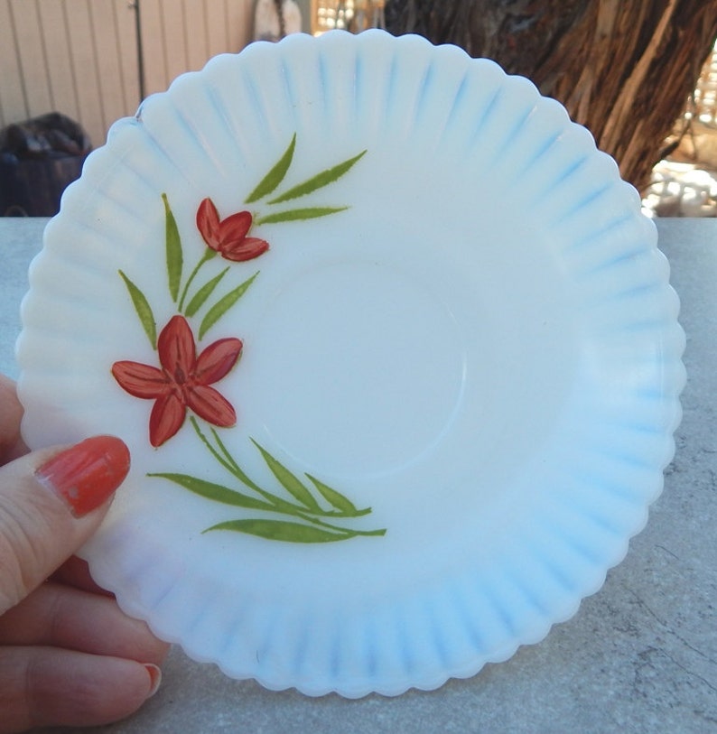 May include: White milk glass saucer with a blue rim and a hand-painted design of red flowers and green leaves.