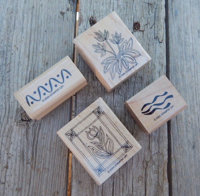 Peut inclure: Quatre tampons en caoutchouc en bois avec des motifs d'encre noire. Les tampons pr&eacute;sentent une fleur dans un cadre, des lignes ondul&eacute;es, une fleur avec des feuilles et une s&eacute;rie de points. Chaque tampon comprend le texte "&copy;2004 STAMPIN' UPI" ou "&copy;2002 STAMPIN' UPI" ou "&copy;2005 STAMPIN' UPI".