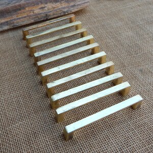 May include: A collection of ten brass cabinet pulls arranged on a textured, tan surface. Each pull is rectangular with a simple, modern design. The pulls are a warm, golden color, reflecting light.