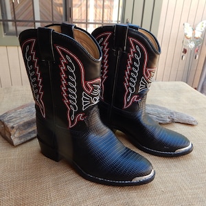 May include: A pair of black leather cowboy boots with red and white stitching. The boots have a pointed toe and a silver cap on the toe.
