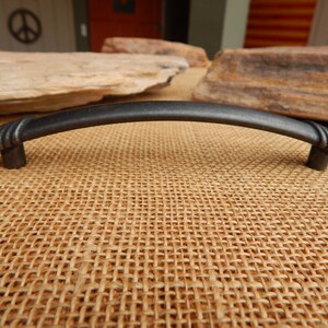 May include: A black metal cabinet pull with a curved design. The pull has a smooth, slightly textured finish.