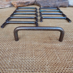 May include: Ten antique bronze drawer pulls with a simple, curved design. The pulls are arranged in two rows of five, with the bottom row slightly offset from the top row.