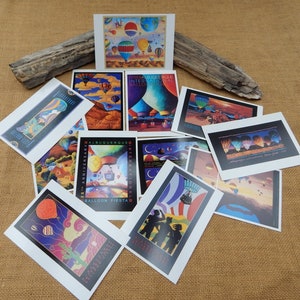 May include: A collection of colorful postcards featuring hot air balloons. The postcards depict various scenes, including a cityscape, a desert landscape, and a night sky. The text on the postcards reads "Albuquerque International Balloon Fiesta".