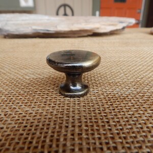 May include: A round, brass cabinet knob with a slightly textured finish. The knob has a short, cylindrical stem.