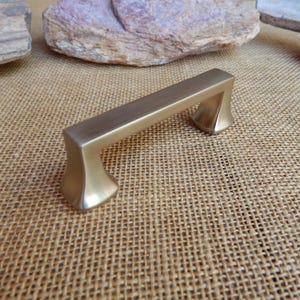 May include: A brushed nickel cabinet pull with a rectangular shape and rounded edges. The pull has a contemporary style.