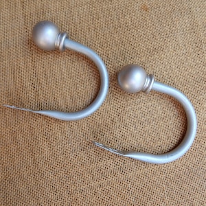 May include: Two silver curtain hooks with round ball finials. The hooks are made of metal and have a smooth finish.