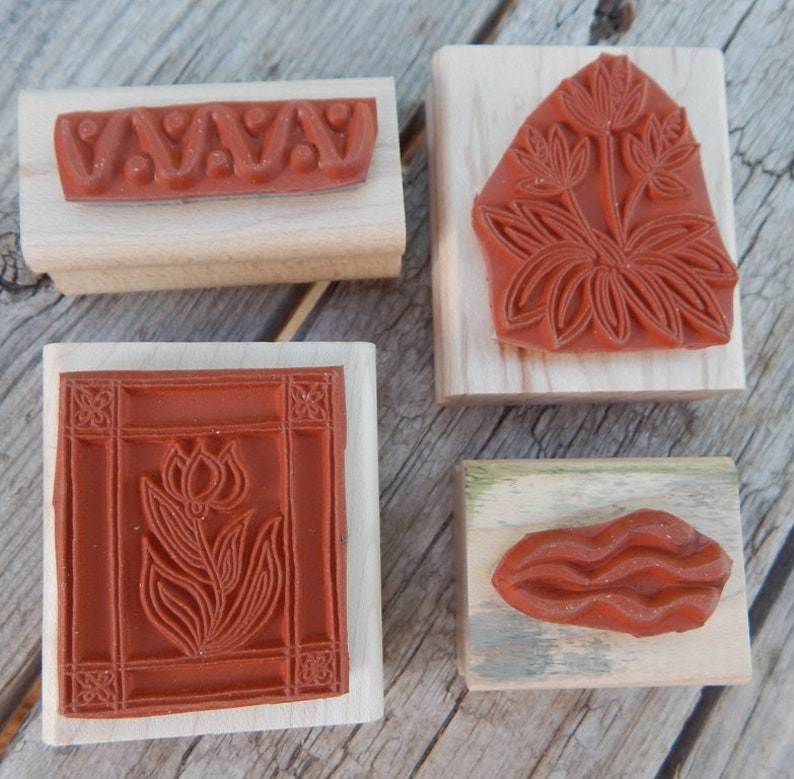 Peut inclure: Quatre blocs de bois avec diff&eacute;rents tampons en caoutchouc rouge. Les tampons pr&eacute;sentent une ligne ondul&eacute;e, une fleur stylis&eacute;e, un motif floral et une ligne ondul&eacute;e.