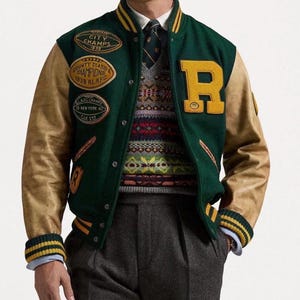 May include: A green varsity jacket with tan leather sleeves, yellow striped ribbed cuffs, and a large yellow letter R patch. The jacket features multiple embroidered patches including City Champs 1939, County Class Champions 1939, and New York 40. Worn over a patterned sweater, tie, and gray trousers.
