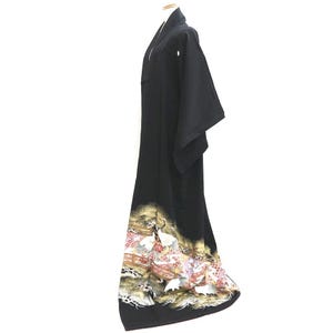 May include: A black kimono with a decorative hem featuring a landscape with cranes, bridges, and floral elements in gold, white, and red. The kimono is displayed on a mannequin, showcasing its flowing design.